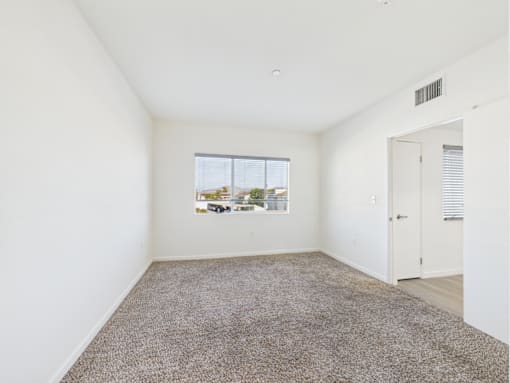 A room with a carpeted floor and a window showing a parking lot outside.