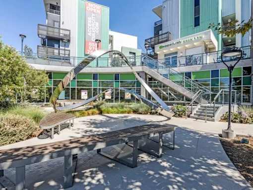 A modern outdoor seating area with a metal bench and a glass wall in the background.