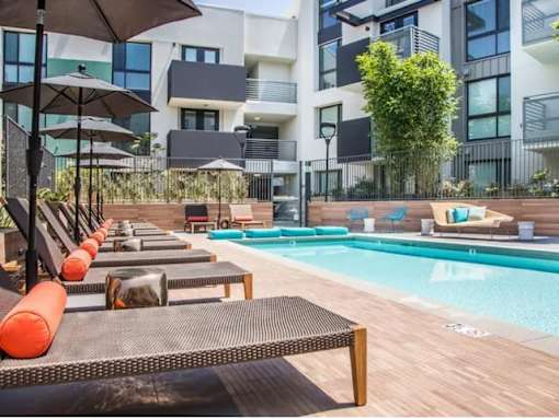 A pool area with sun loungers and umbrellas in front of a modern building.