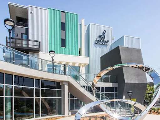 A modern building with a glass facade and a large metal sculpture in front.