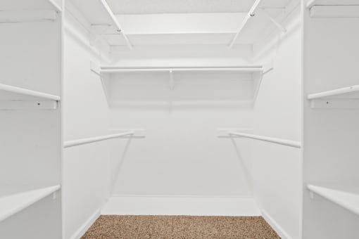 a walk in closet with white walls and white shelves