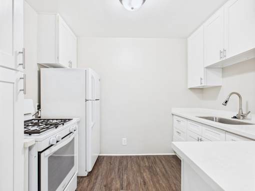 A white kitchen with a stove, refrigerator, and cabinets.