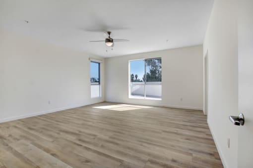 an empty living room with a large window and a ceiling fan