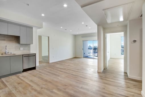 an empty living room with a kitchen and a balcony