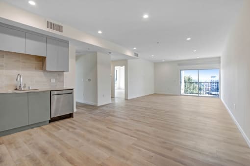 an empty living room with a kitchen and a balcony