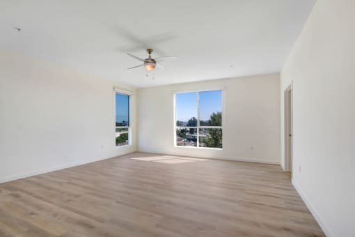 an empty living room with a large window and a ceiling fan