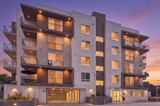 A modern apartment building with balconies and a person walking in front.