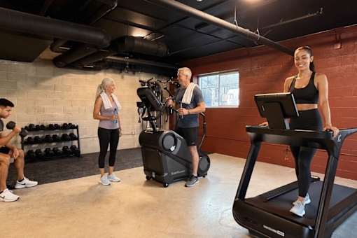 A woman is standing on a treadmill in a gym with other people around her.