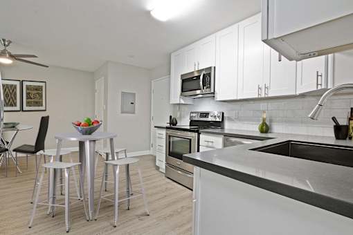 Open kitchen with stainless steel electric stove with micro hood microwave, tile backsplash, white kitchen cabinets, gray quartz counters