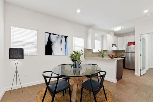 a dining area with a glass table and chairs and a kitchen in the background