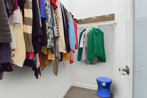 a closet with a rack of clothes and a blue stool