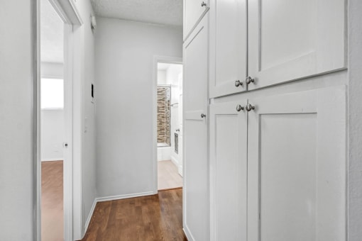 an empty room with white cabinets and a hallway with a door to a kitchen