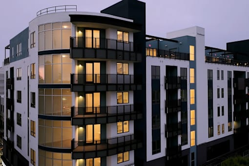A modern building with black and white balconies is illuminated at dusk.