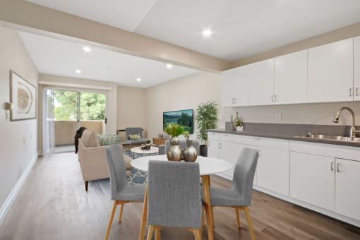 a kitchen and living room with white cabinets and a white dining table with grey chairs