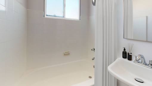 A white bathroom with a tub, sink, and window.