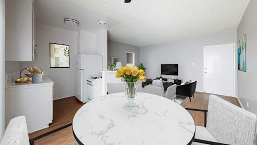 A white marble table with a vase of yellow flowers is in the middle of a modern kitchen and dining room.