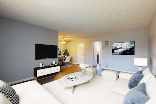 A living room with a white couch and a flat screen TV mounted on the wall.