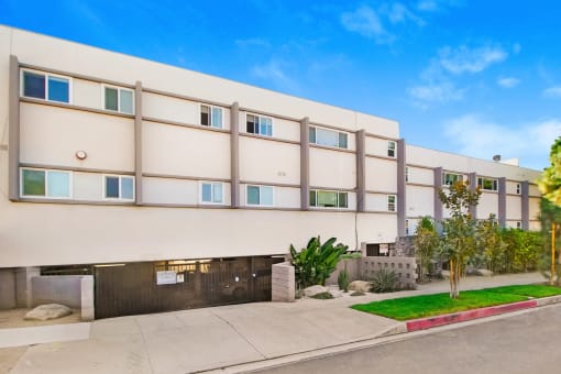 a white apartment building with a sidewalk and grass in front of it
