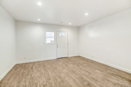 a living room with white walls and wood flooring and a white door
