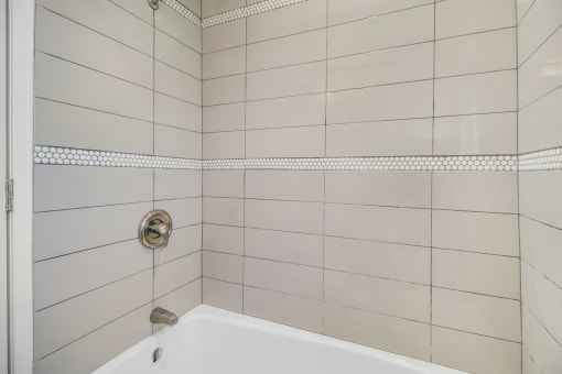 a white tiled bathroom with a tub and shower