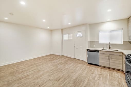 the living room and kitchen of an apartment with a wooden floor and white walls