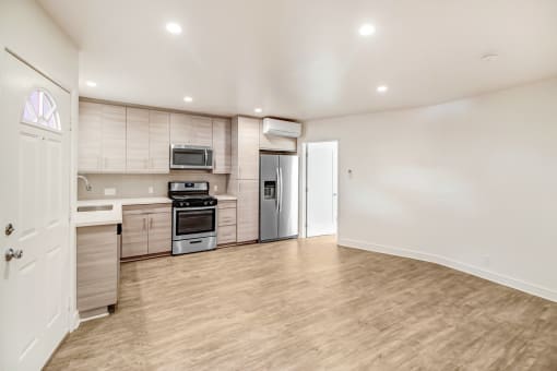 an empty living room with a kitchen with stainless steel appliances