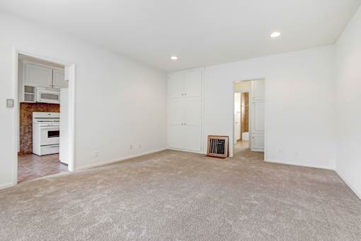 an empty living room with white walls and a white kitchen