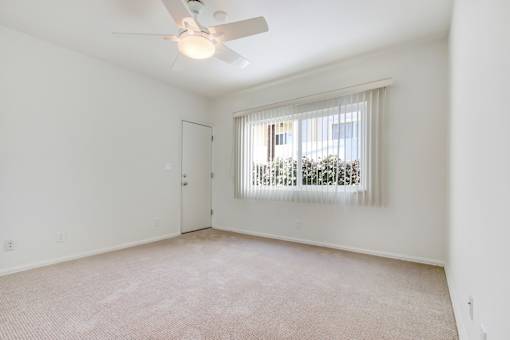 an empty living room with a window and a ceiling fan