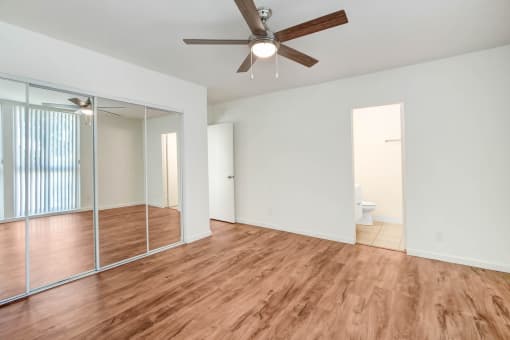 an empty living room with a ceiling fan and a mirrored closet