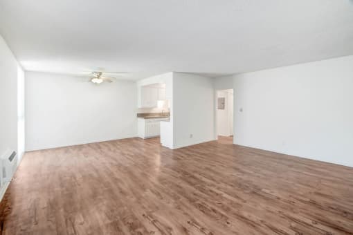 the living room and kitchen of an apartment with wood flooring and a ceiling fan