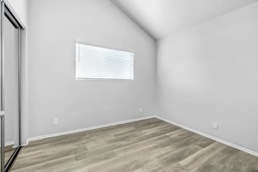 a bedroom with white walls and wood flooring and a window