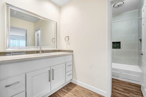 a bathroom with white cabinets and a large mirror and a shower