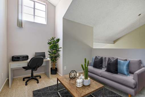A room with a couch, desk, and potted plant.