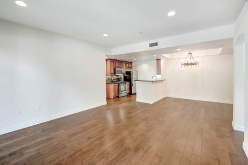 an empty living room and kitchen with wood flooring and a chandelier