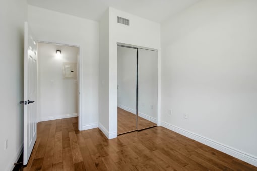 a bedroom with white walls and wood floors and a mirrored closet