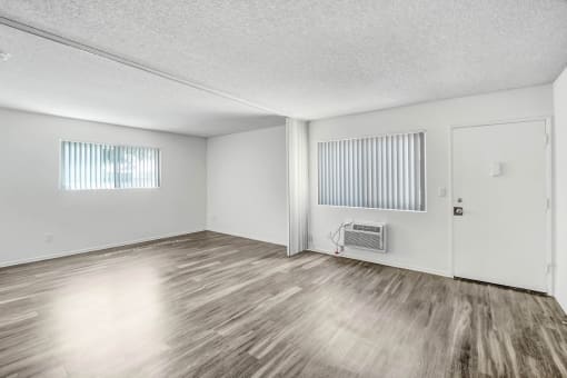 the spacious living room of an apartment with wood flooring and white walls