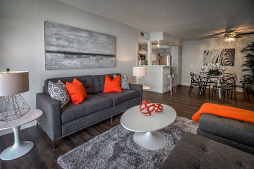 A grey couch with orange pillows sits in a living room with a white coffee table in front of it.