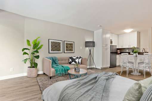 Sleeping and living area of a studio unit with wood-inspired floors throughout, stainless steel kitchen appliances