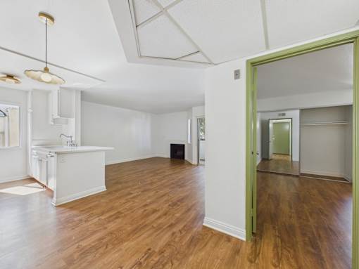 A room with a white kitchen and wooden floors.