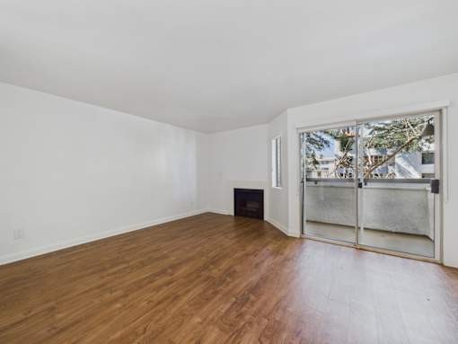 A room with wooden flooring and a window with a view of trees and buildings outside.