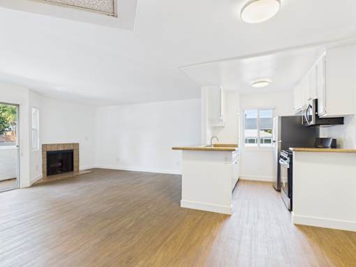 A spacious kitchen and living room with wood flooring and white walls.