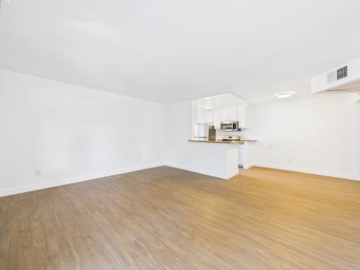 A room with wooden flooring and a kitchenette in the corner.