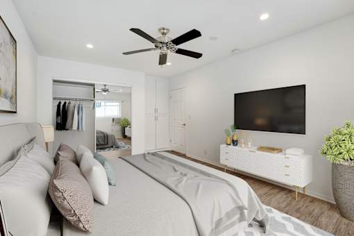 A bedroom with a bed, a couch, a TV, and a plant.