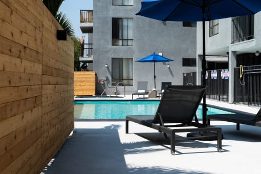 a pool with two lounge chairs and umbrellas in front of a building