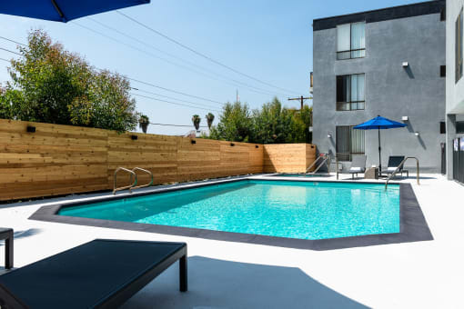 a pool in a backyard with a wooden fence and a gray building in the background