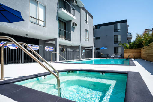 a swimming pool with a blue umbrella in front of an apartment building