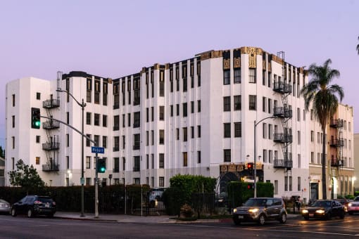 a white building on the corner of a street with cars driving in front of it