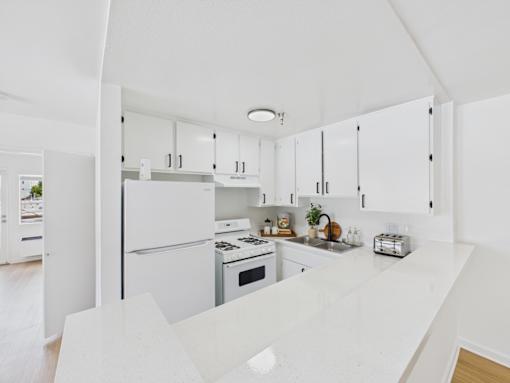 A white kitchen with a refrigerator, oven, and sink.
