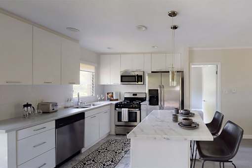 A modern kitchen with a white marble island and black chairs.