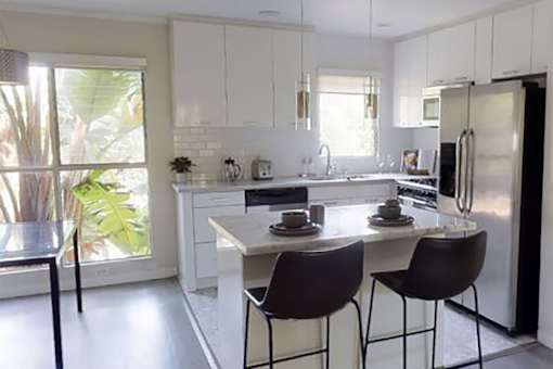A kitchen with white cabinets and a large island with two chairs.
